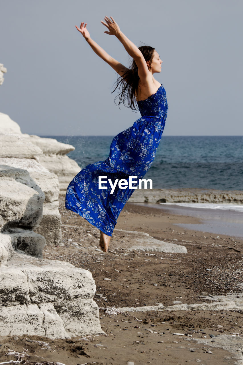 Young woman jumping at beach against clear sky