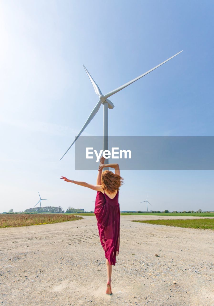 Rear view of woman dancing against windmill during sunny day