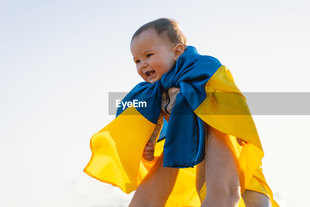 Little boy wrapped in yellow and blue flag of ukraine in outdoors. independence day.