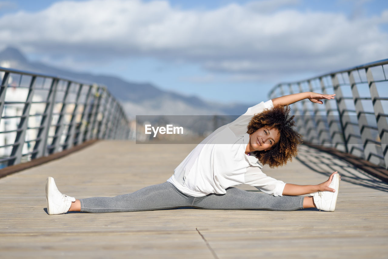 Full length of young woman exercising on bridge against sky