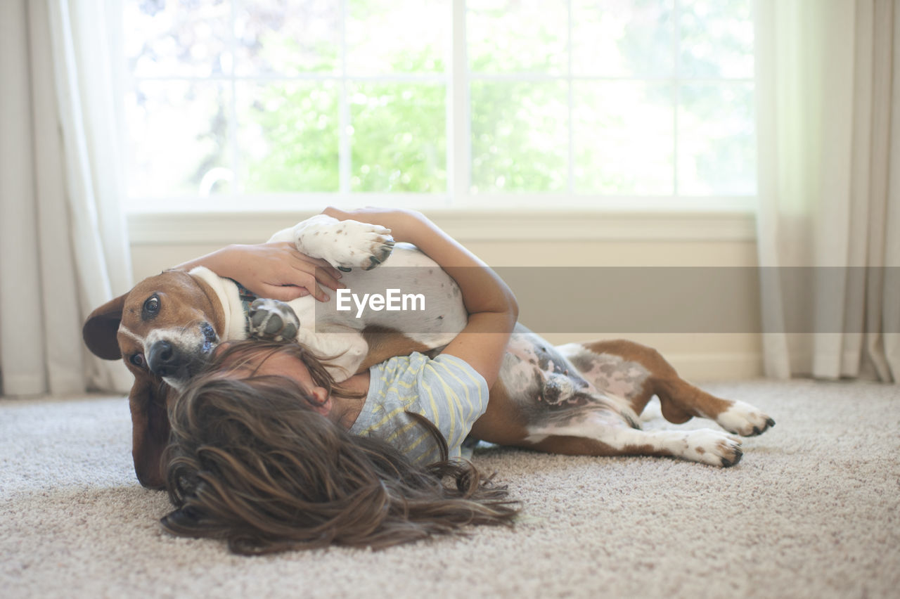 Young girl laying with her basset hound dog on the floor at home