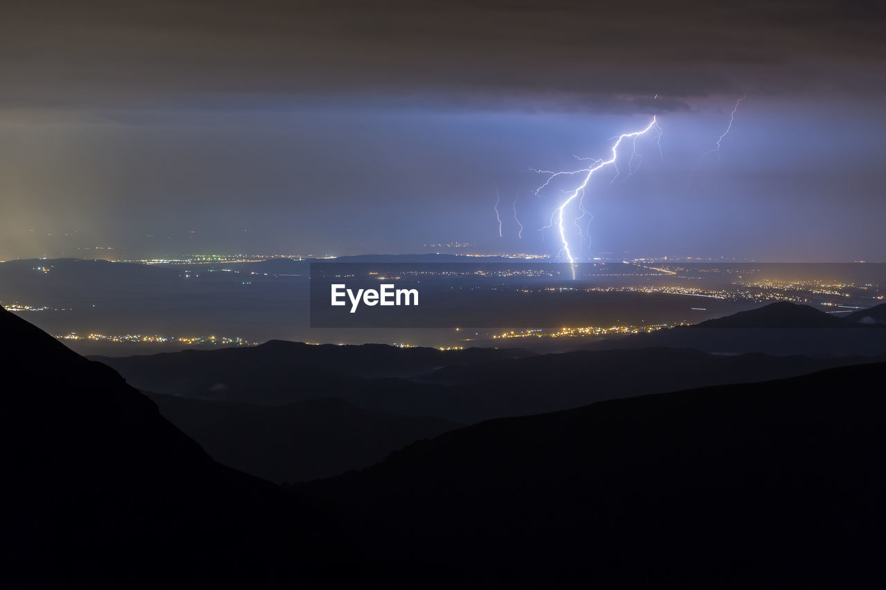 Panoramic view of lightning over mountains against sky at night