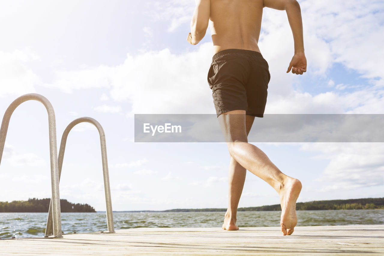 Low section of man running on boardwalk at lake