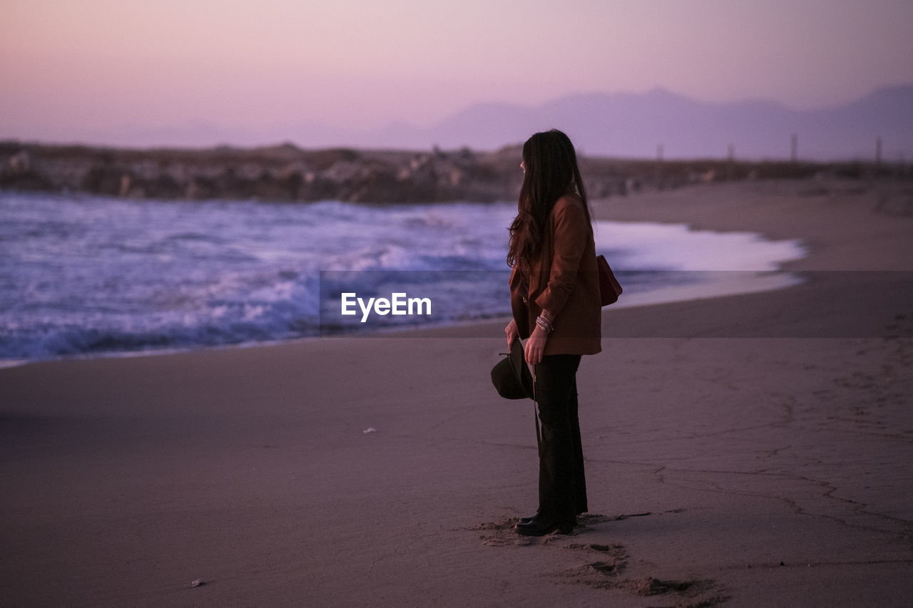 Woman standing at beach during sunset