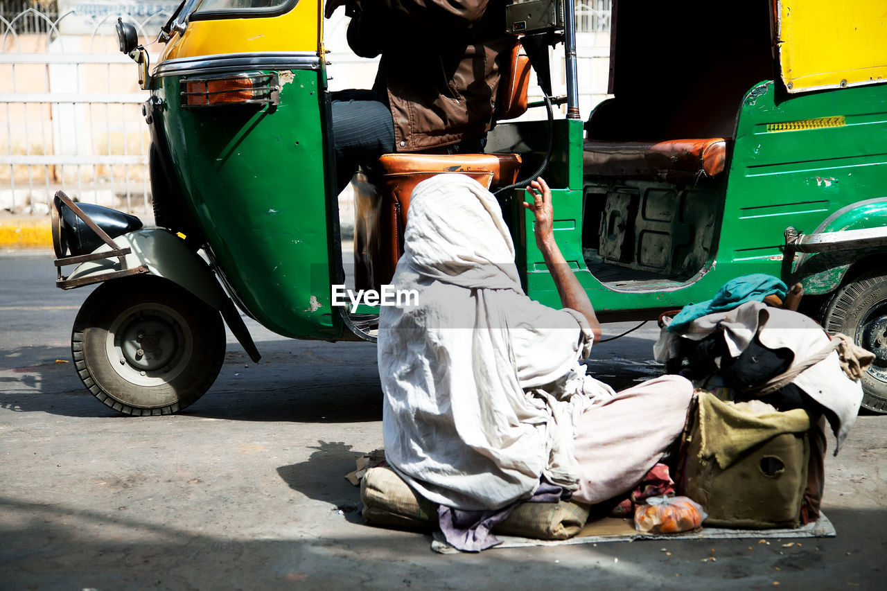 Beggar begging in front of auto rickshaw on street