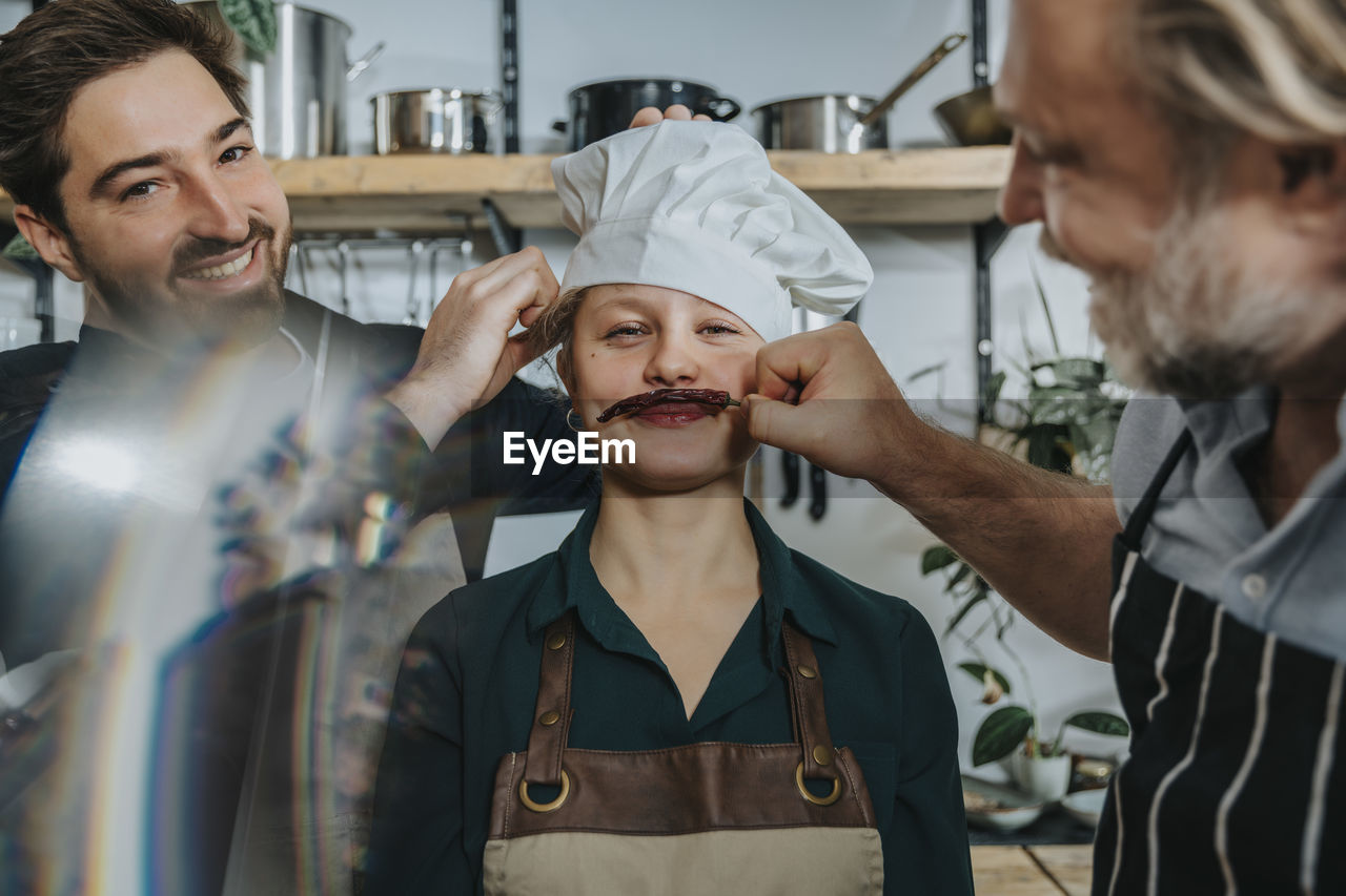 Chefs having fun with young colleague while standing in kitchen