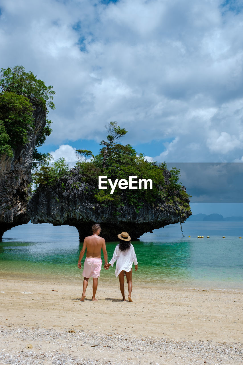 rear view of people walking on beach against sky