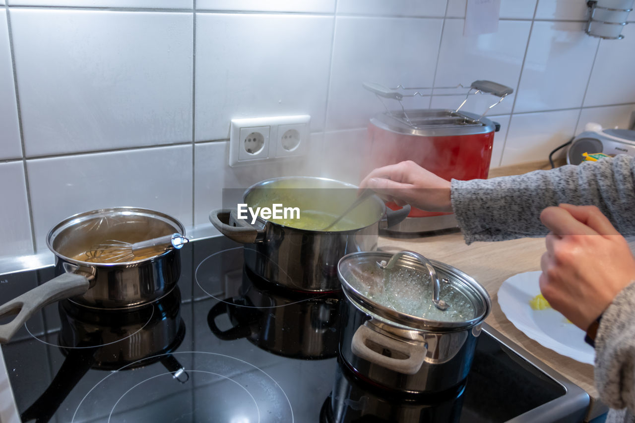 Woman cooking on cooker in the kitchen with hot steam and pots on a ceran stove to cook