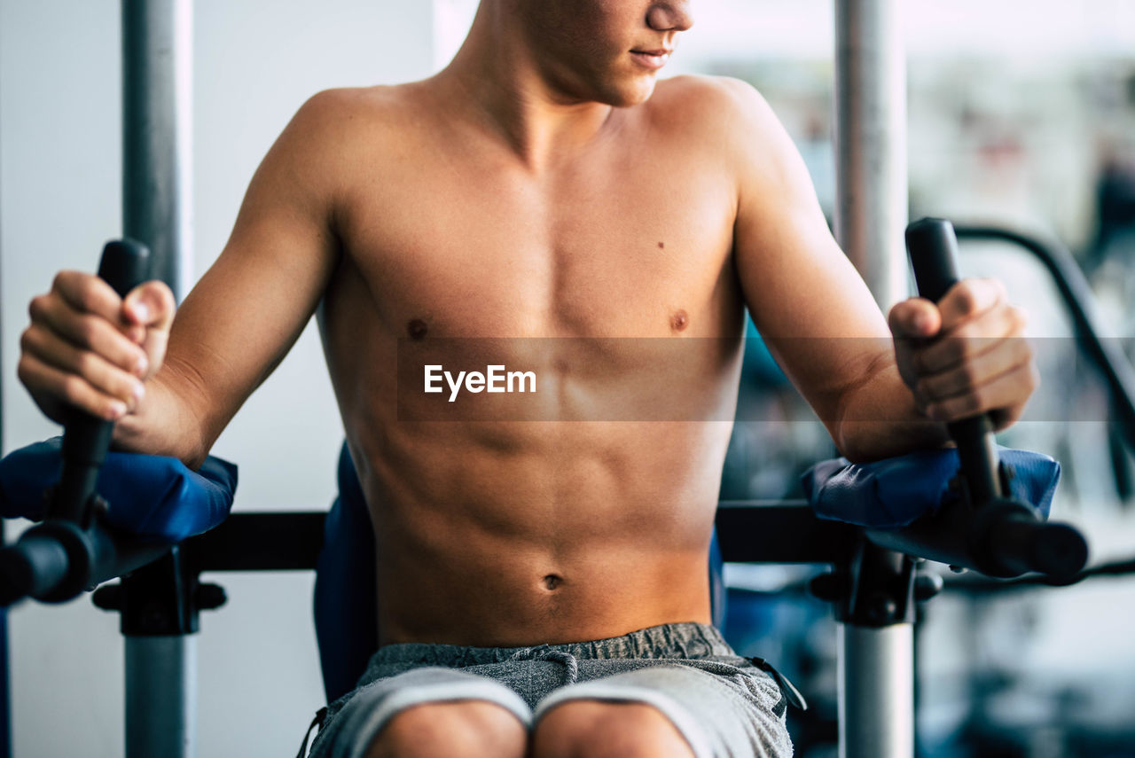 Midsection of shirtless teenage boy exercising at gym