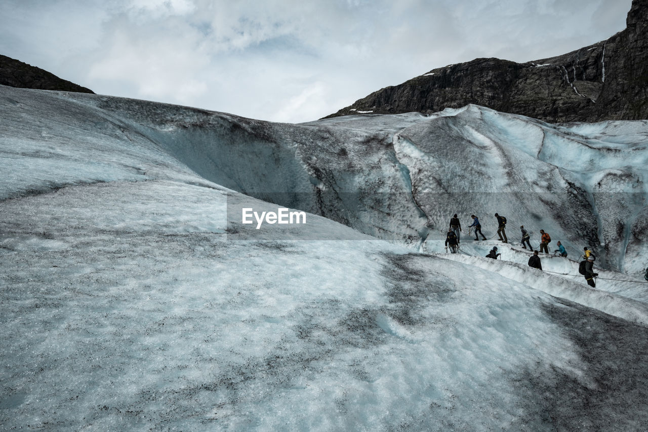 People hiking on glacier against cloudy sky