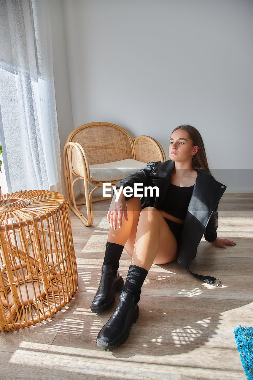 Portrait of young woman sitting on floor at home with black jacket 