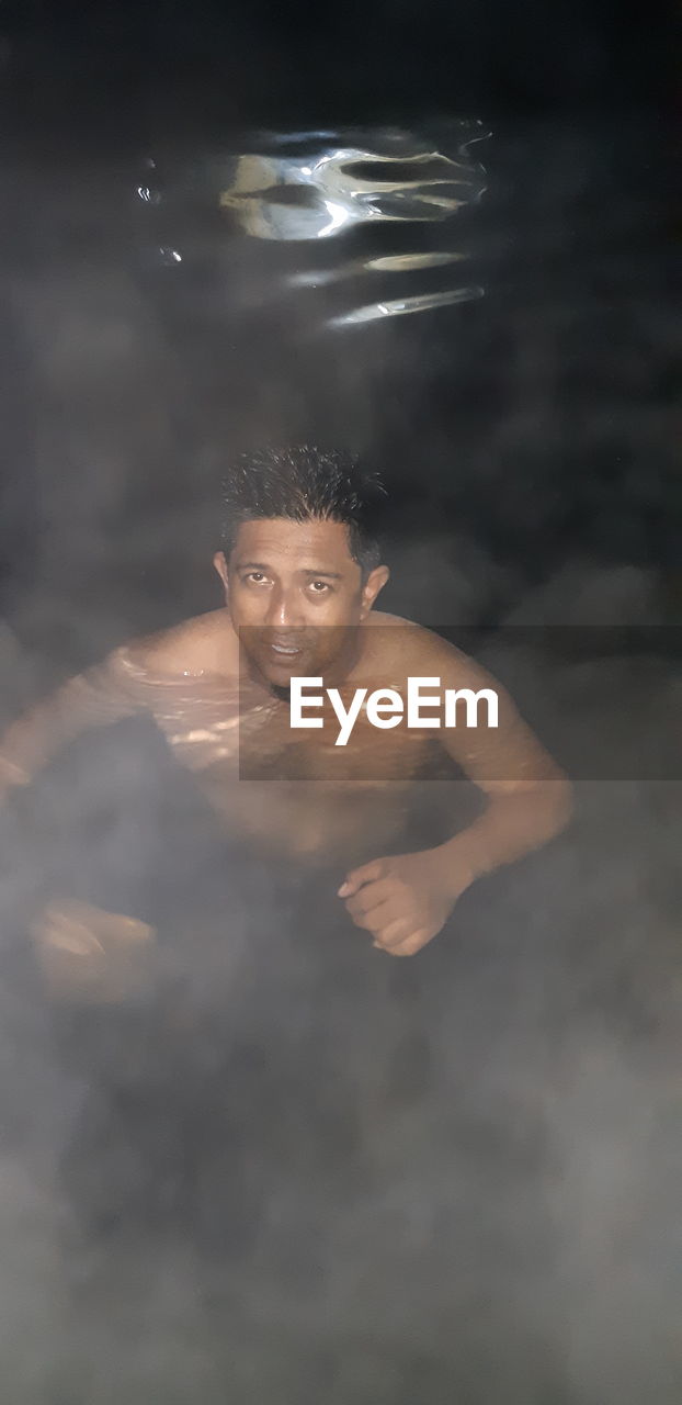 PORTRAIT OF SHIRTLESS MAN SWIMMING IN POOL