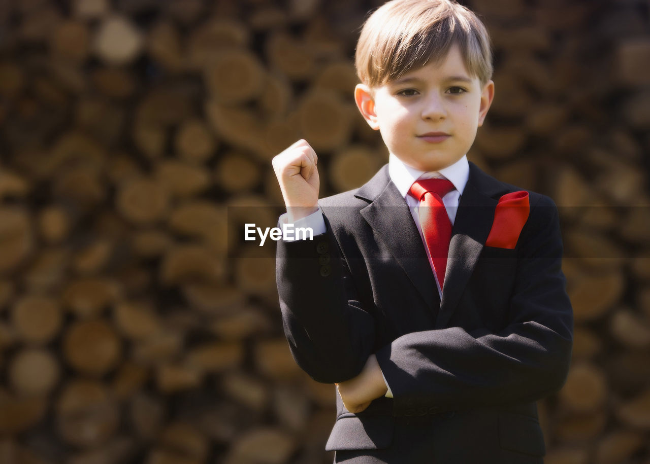 Cute boy wearing suit while looking away against firewood