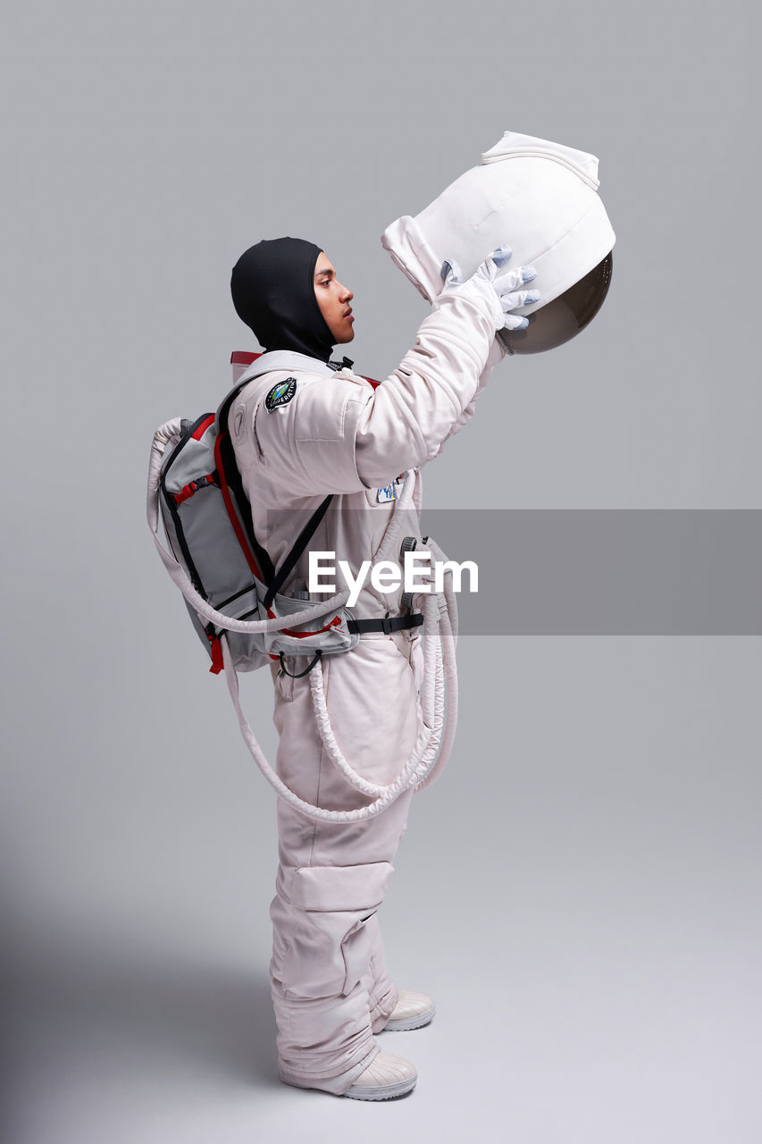 Side view of astronaut in spacesuit taking off protective helmet with visor in studio against white background