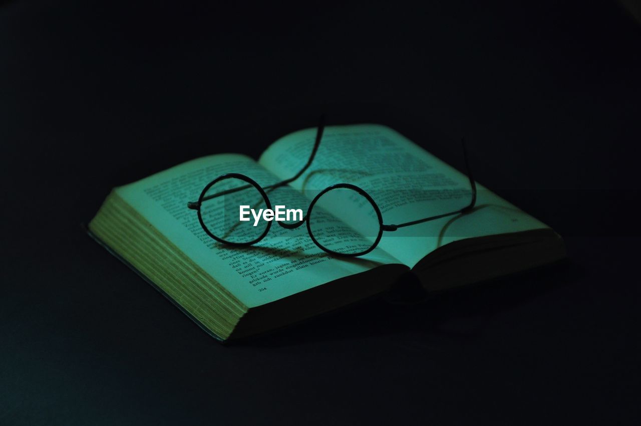 Close-up of open book with eyeglasses against black background