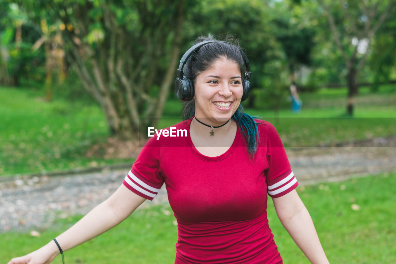 Beautiful college woman with blue hair and red dress listening to music with her wireless headphones