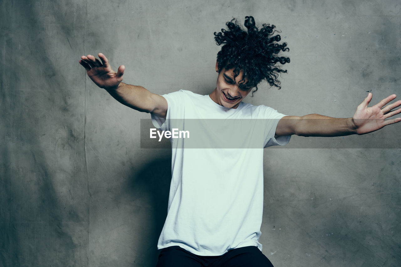 Midsection of man with arms raised standing against wall