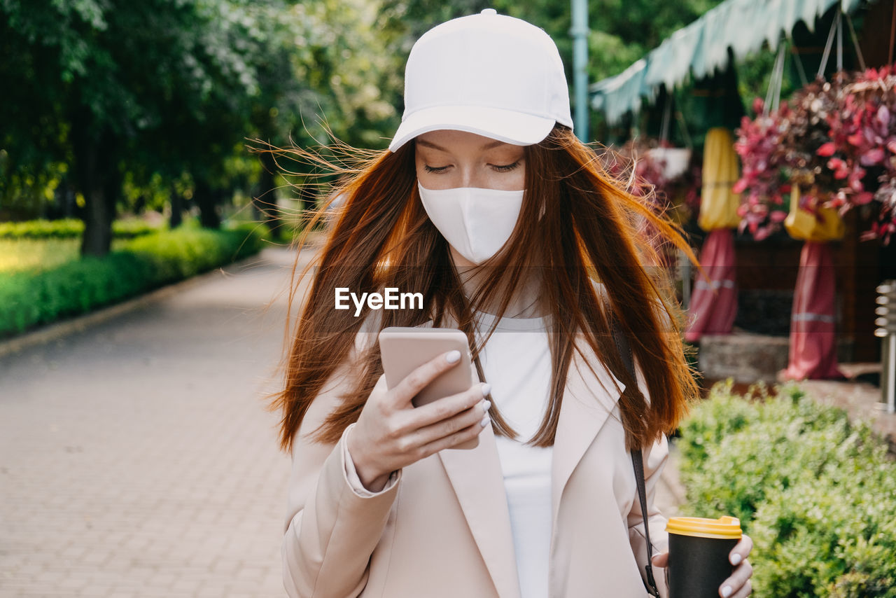 Redhead woman wearing face mask for virus protection. young business woman with cell phone in hand