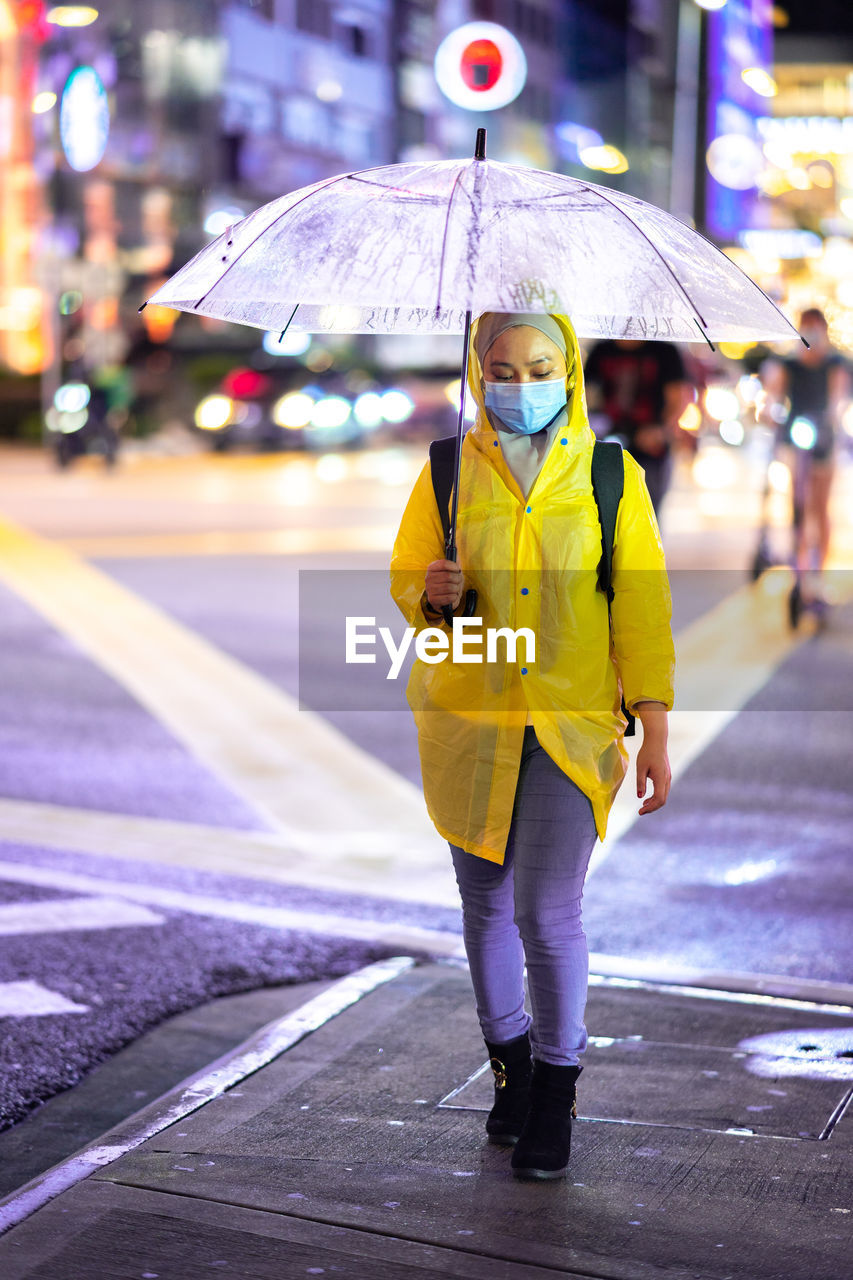 FULL LENGTH OF WOMAN WITH UMBRELLA STANDING ON WET ROAD