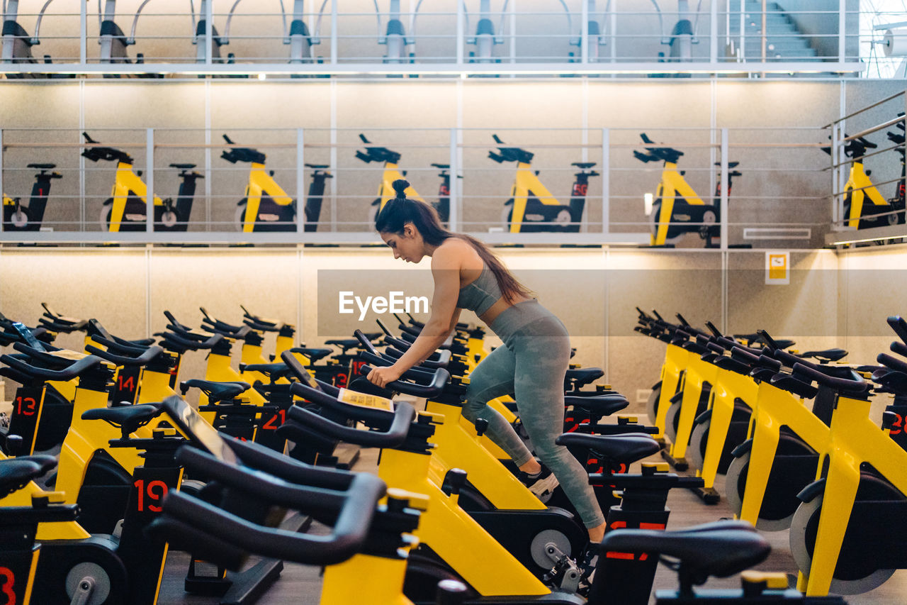 Side view of young female athlete on cardio bike in modern gym