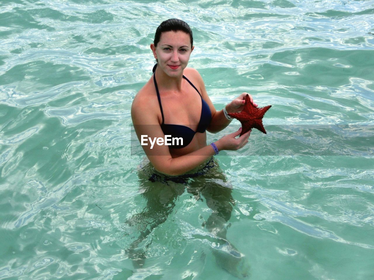 Portrait of woman wearing bikini while holding starfish in sea