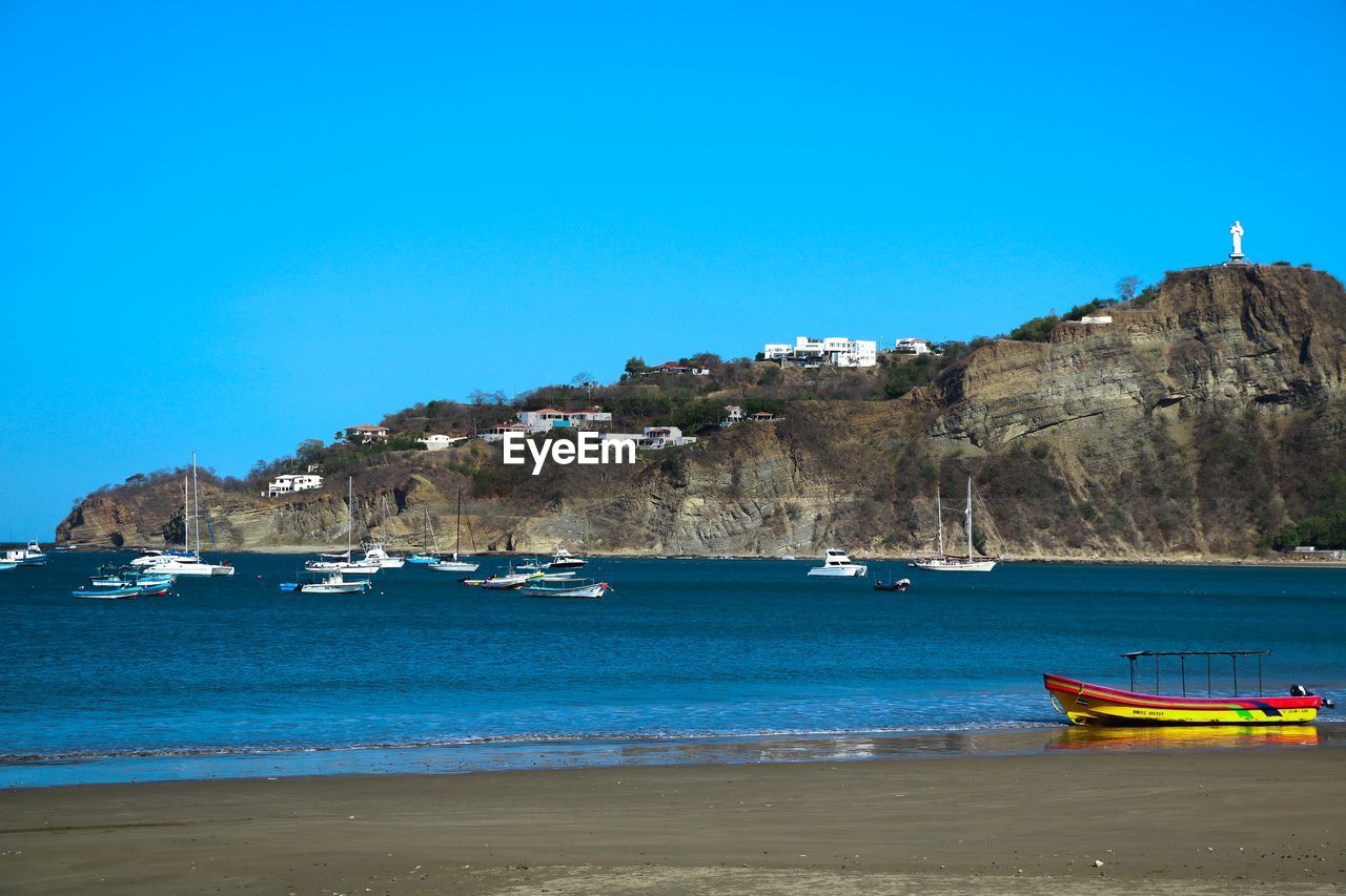 Sailboats moored at harbor against clear blue sky