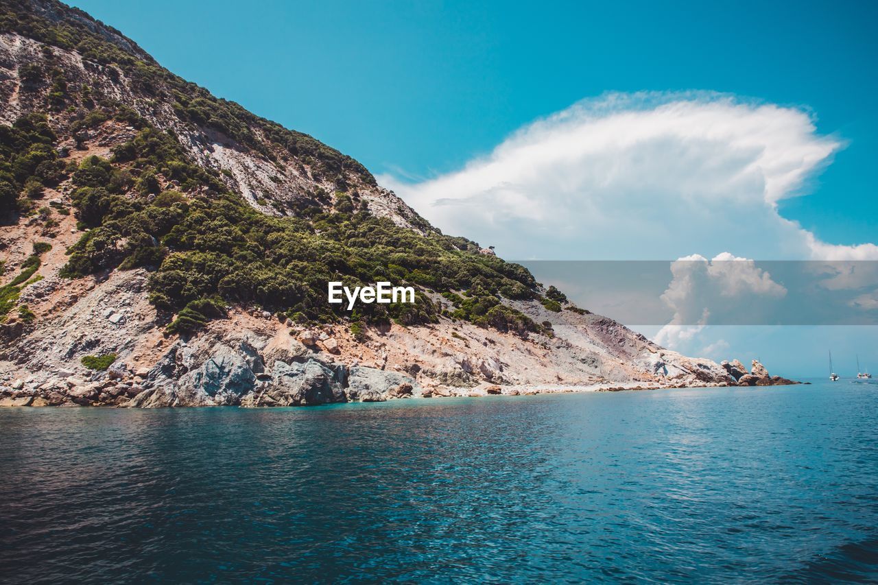 Scenic view of sea by mountain against sky