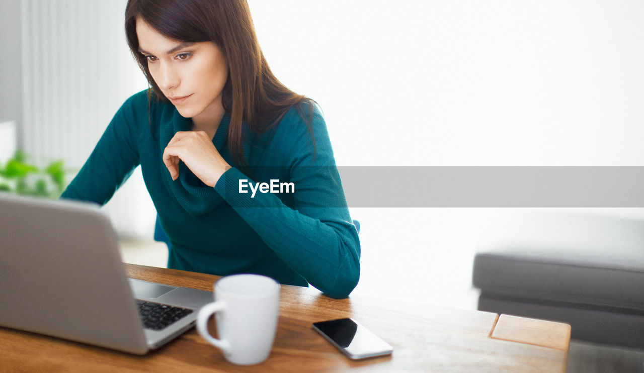 YOUNG WOMAN USING LAPTOP ON TABLE