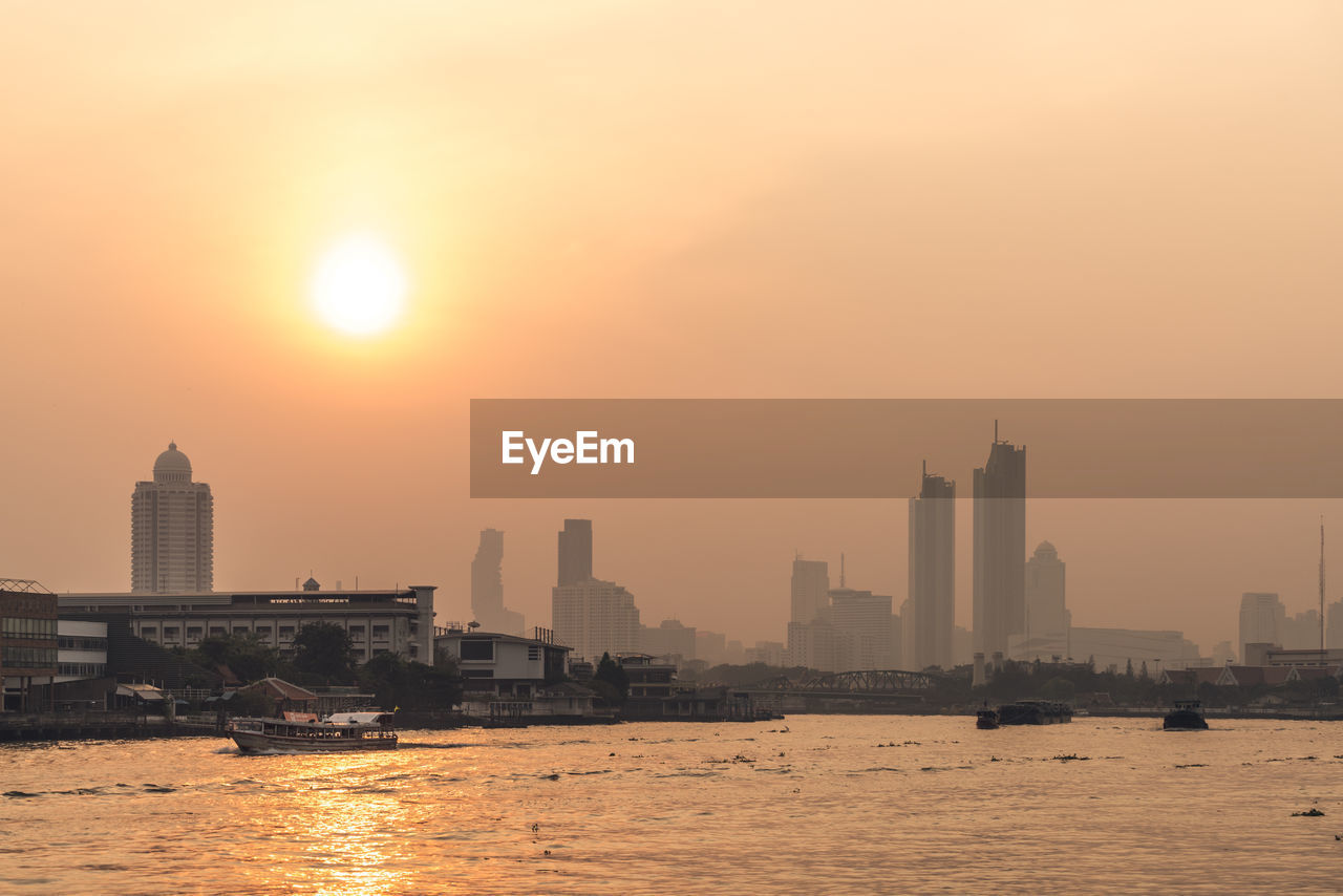 Sea by buildings against sky during sunset