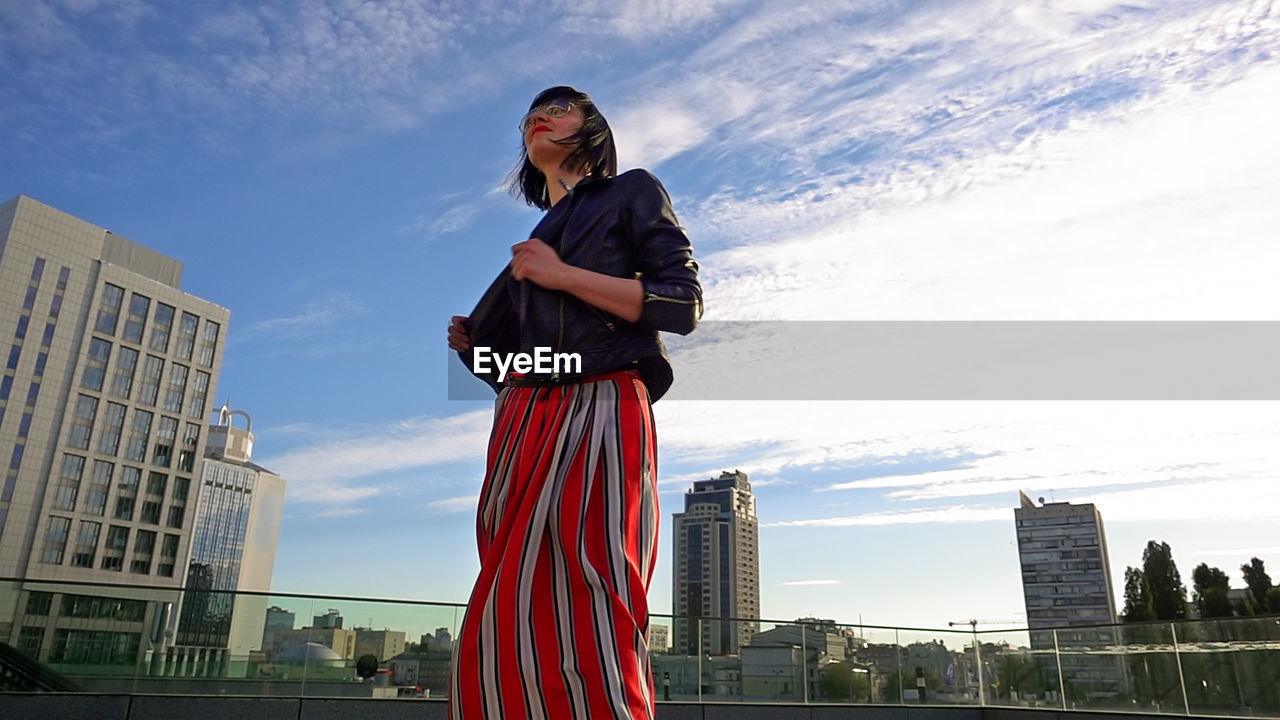 Happy woman wearing striped skirt and jacket on footpath in city