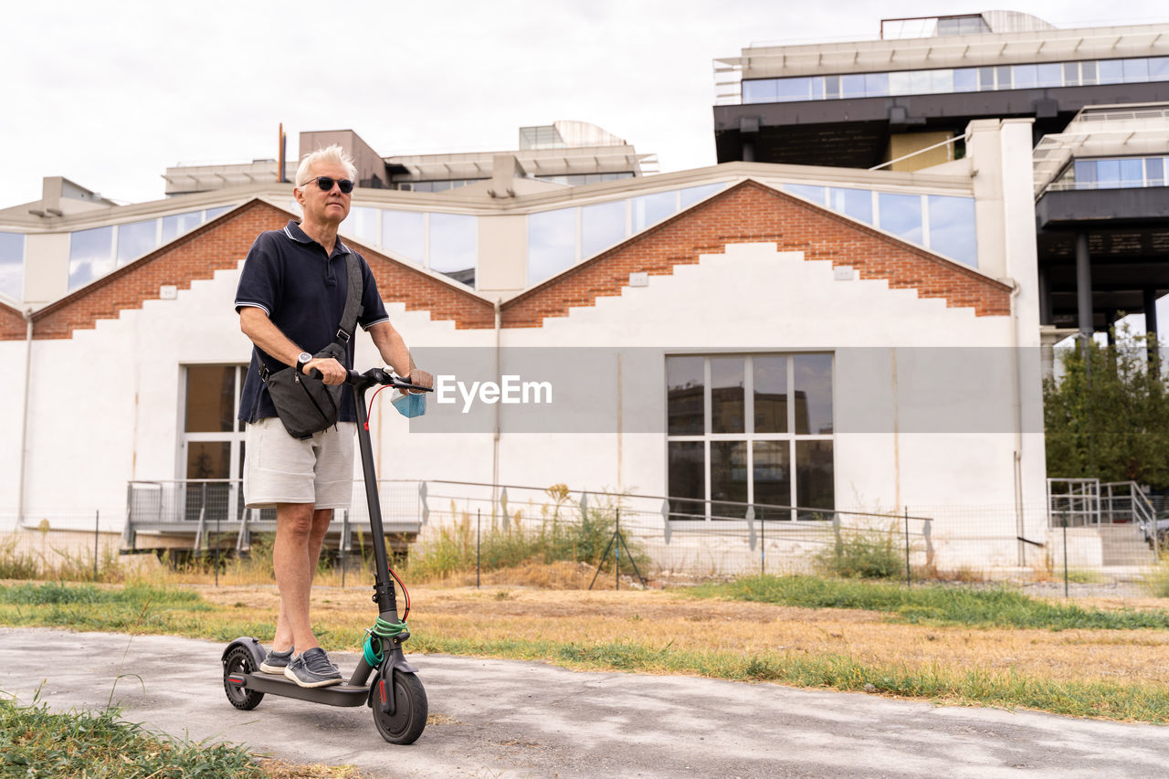 Commuter hipster man is using electric scooter on the outskirts of a city. eco transport concept