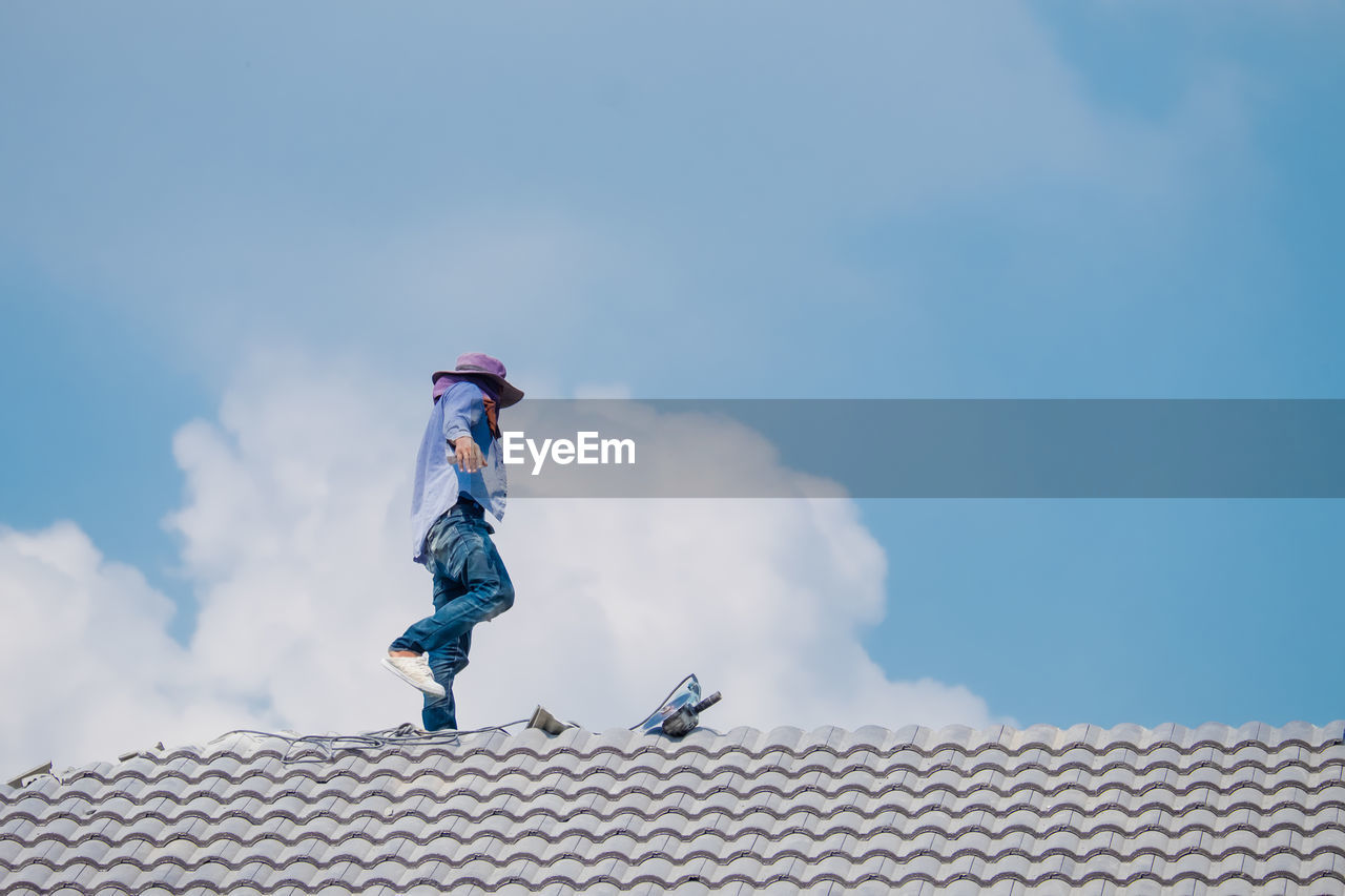 LOW ANGLE VIEW OF MAN ON ROOF OF BUILDING