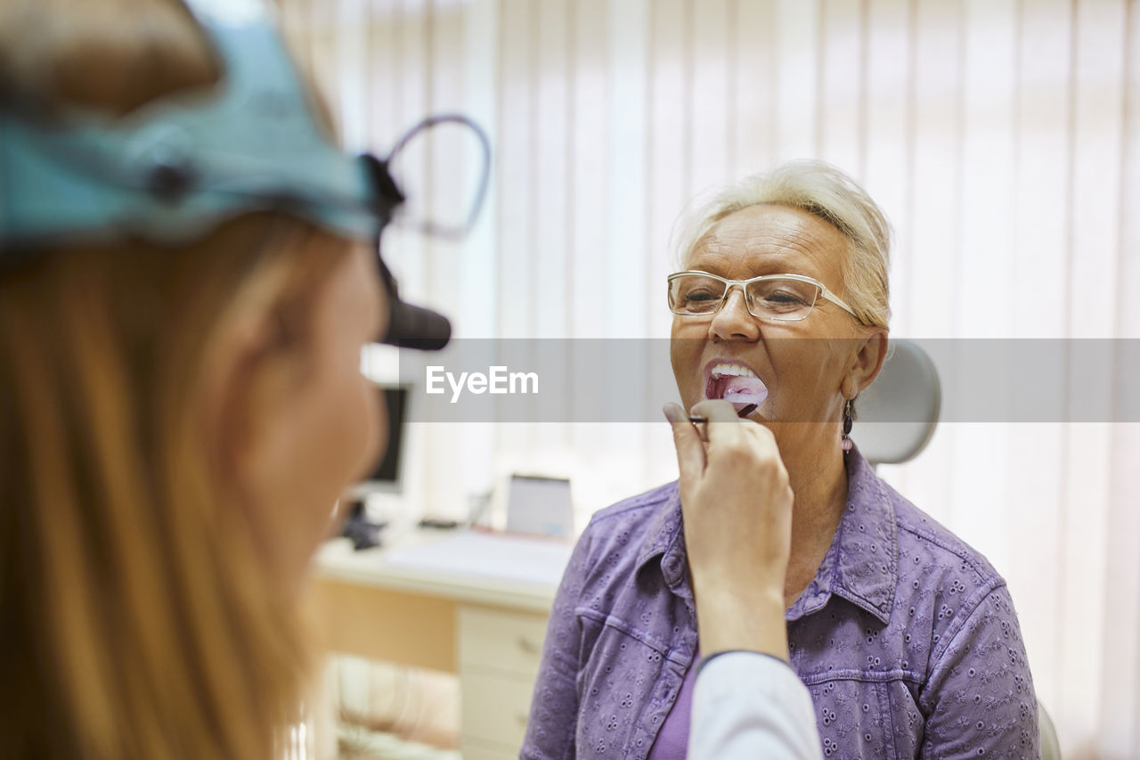 Ent physician examining mouth of a senior woman