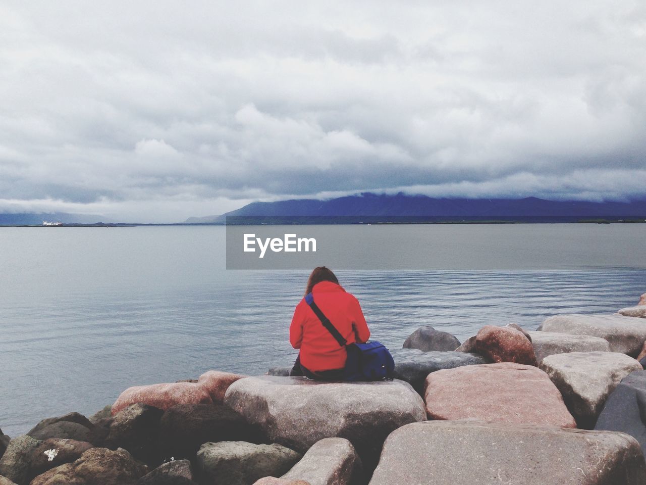 Rear view of woman sitting on rocky beach