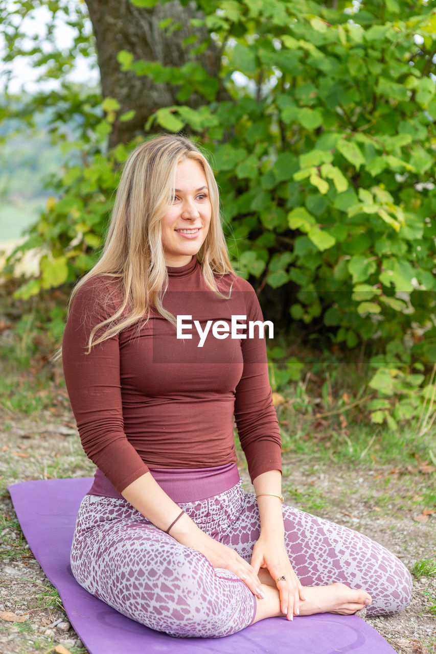 sitting, yoga, women, one person, exercising, adult, wellbeing, blond hair, lifestyles, cross-legged, meditating, zen-like, nature, long hair, relaxation, hairstyle, physical fitness, female, clothing, plant, full length, smiling, leisure activity, sports, person, day, exercise mat, lotus position, spirituality, outdoors, happiness, tranquility, sports clothing, young adult, tree, portrait, posture, stretching, pregnant, front view, casual clothing, flexibility, emotion, arm, human hair, human face, human leg, harmony