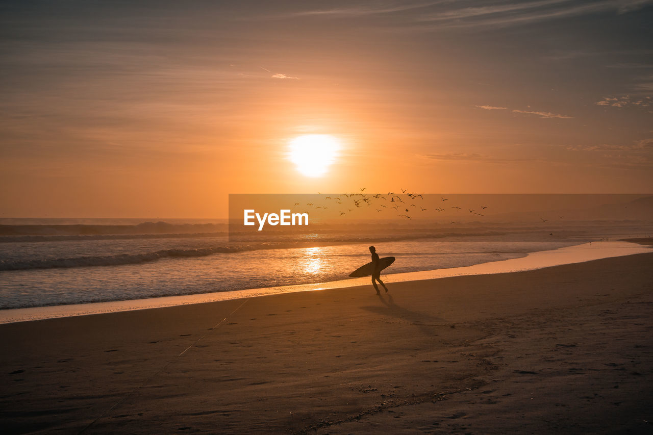 Surfer walking on shore against sea at beach