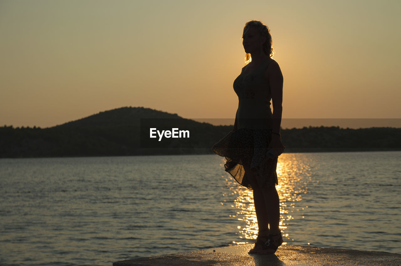 Silhouette woman standing at beach against sky during sunset