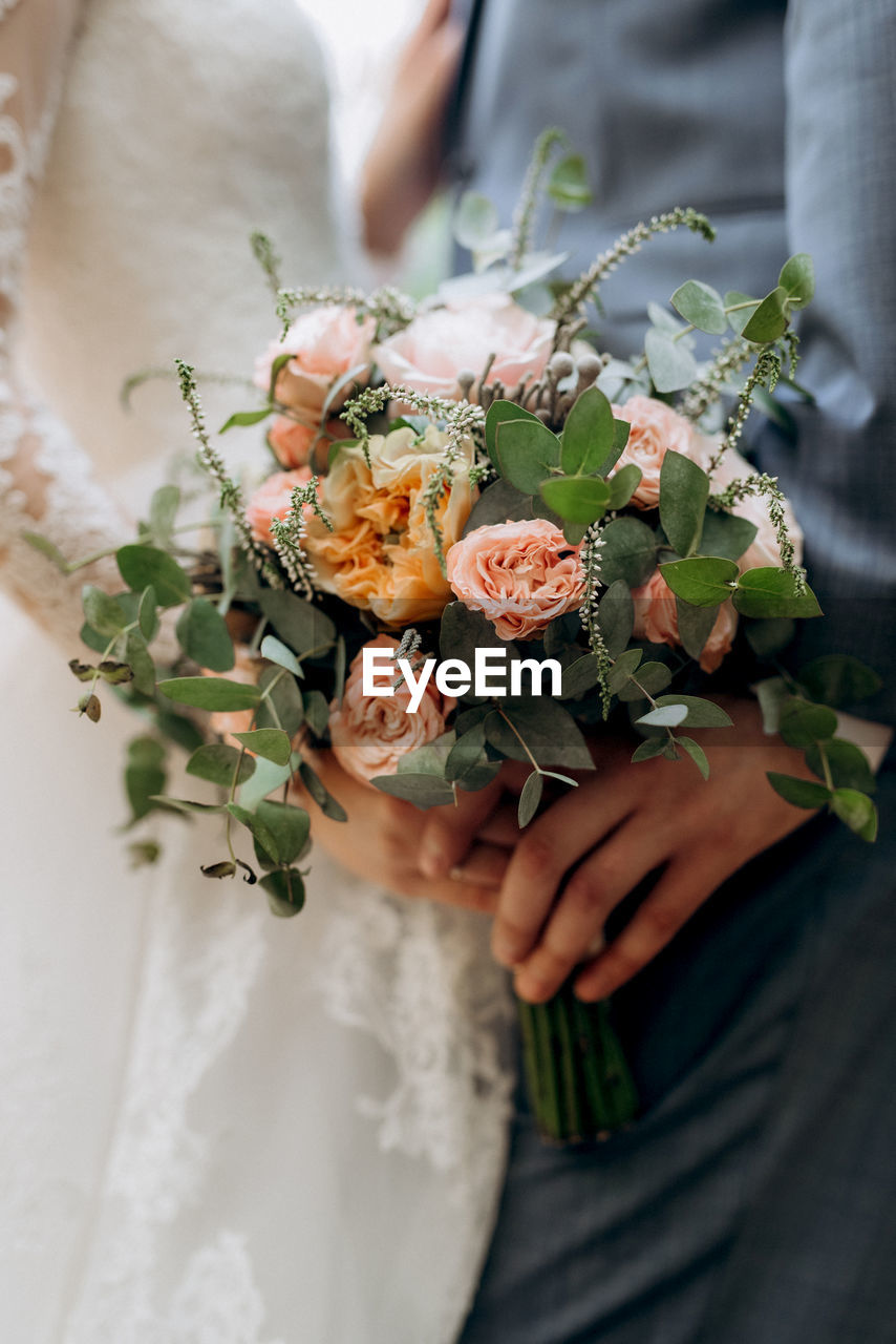 Midsection of bride and groom holding bunch of flowers