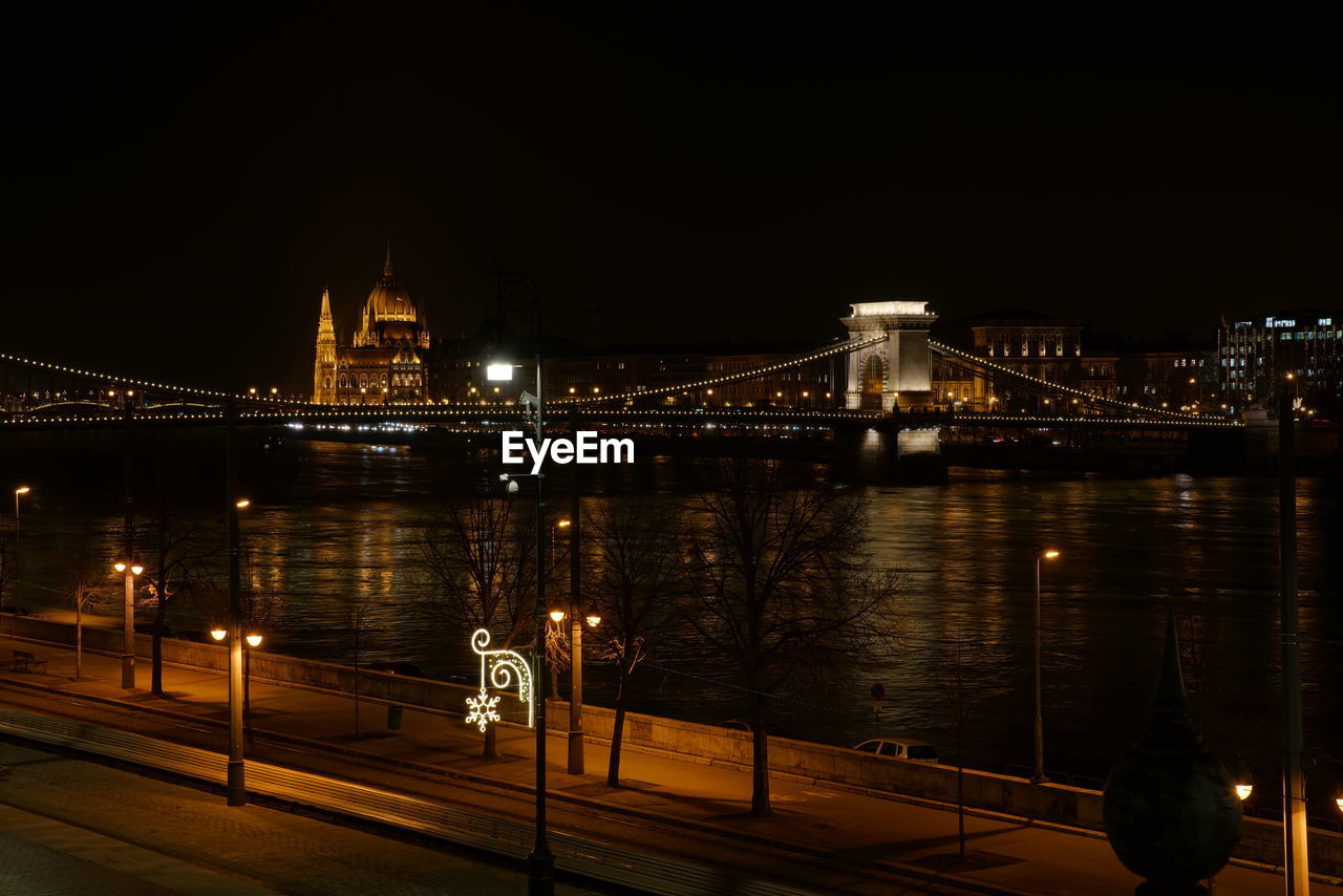 ILLUMINATED BRIDGE OVER RIVER AGAINST SKY