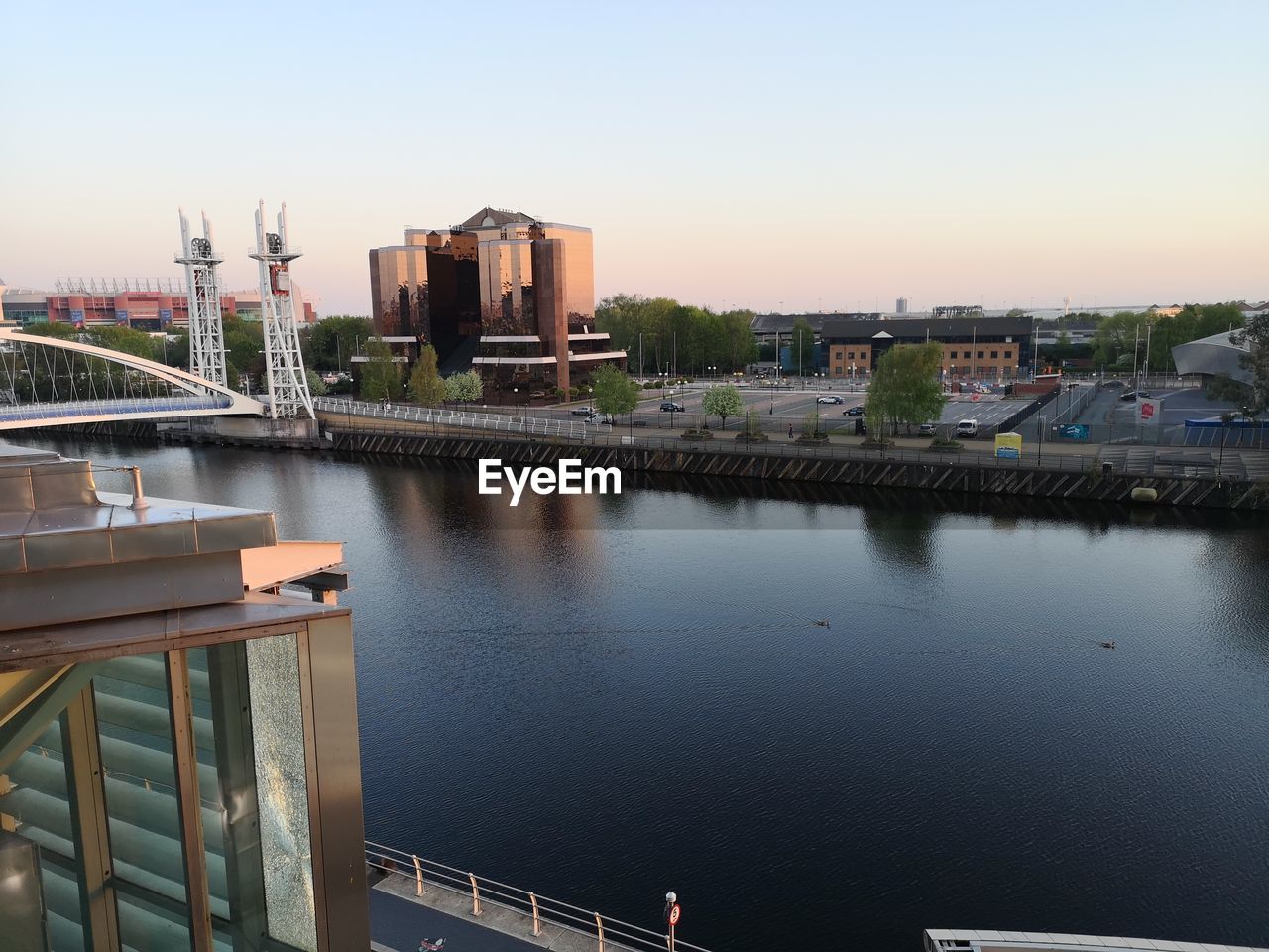 Bridge over river by buildings against sky during sunset