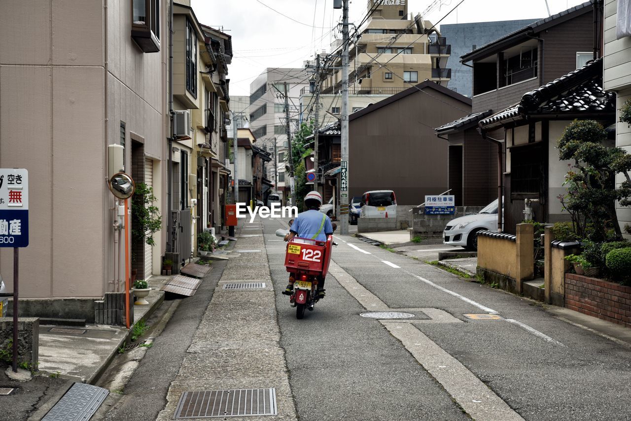 Rear view of man riding motor scooter on road in city