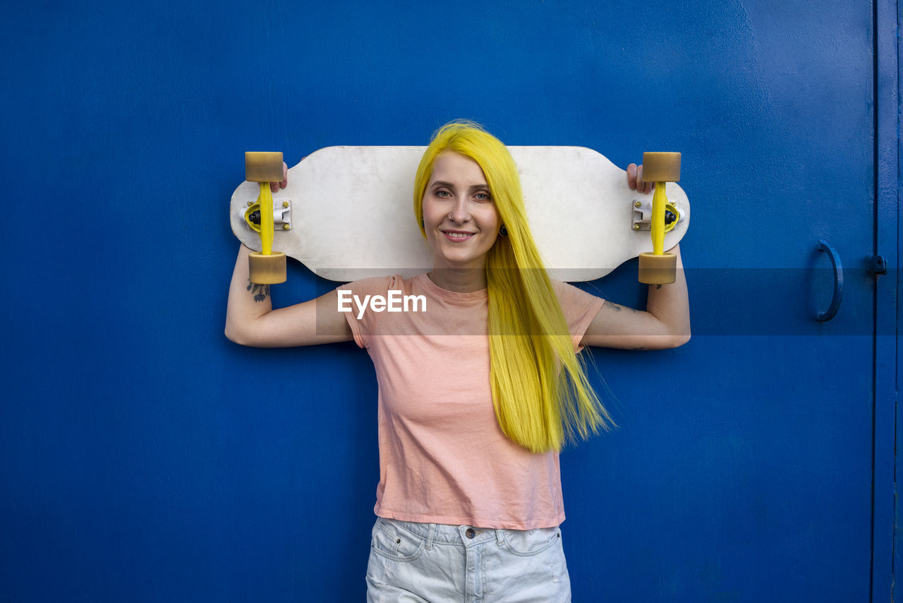 Young woman holding skateboard standing against blue door