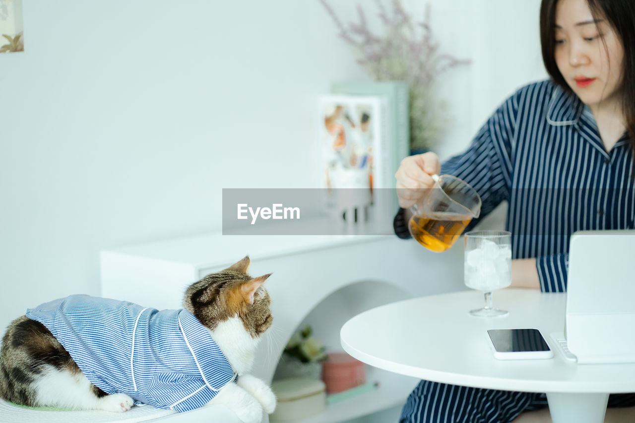 Woman in pajamas cloth drink tea and play with her cat