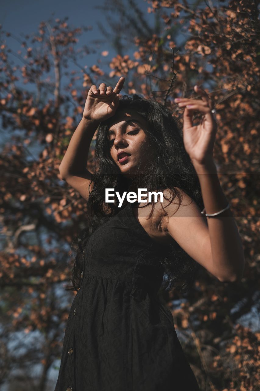 PORTRAIT OF BEAUTIFUL YOUNG WOMAN STANDING AGAINST TREE