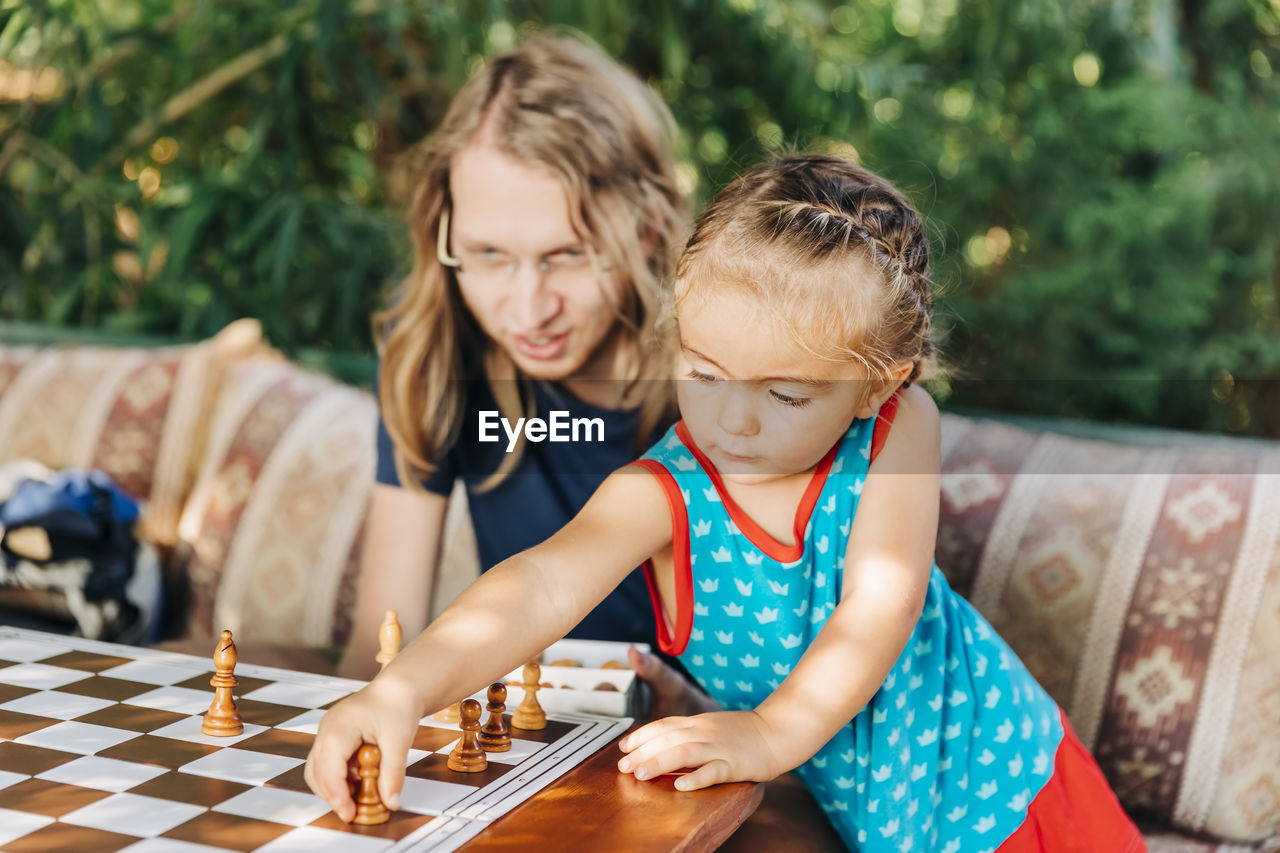 Father teaching chess to daughter while sitting on sofa at home