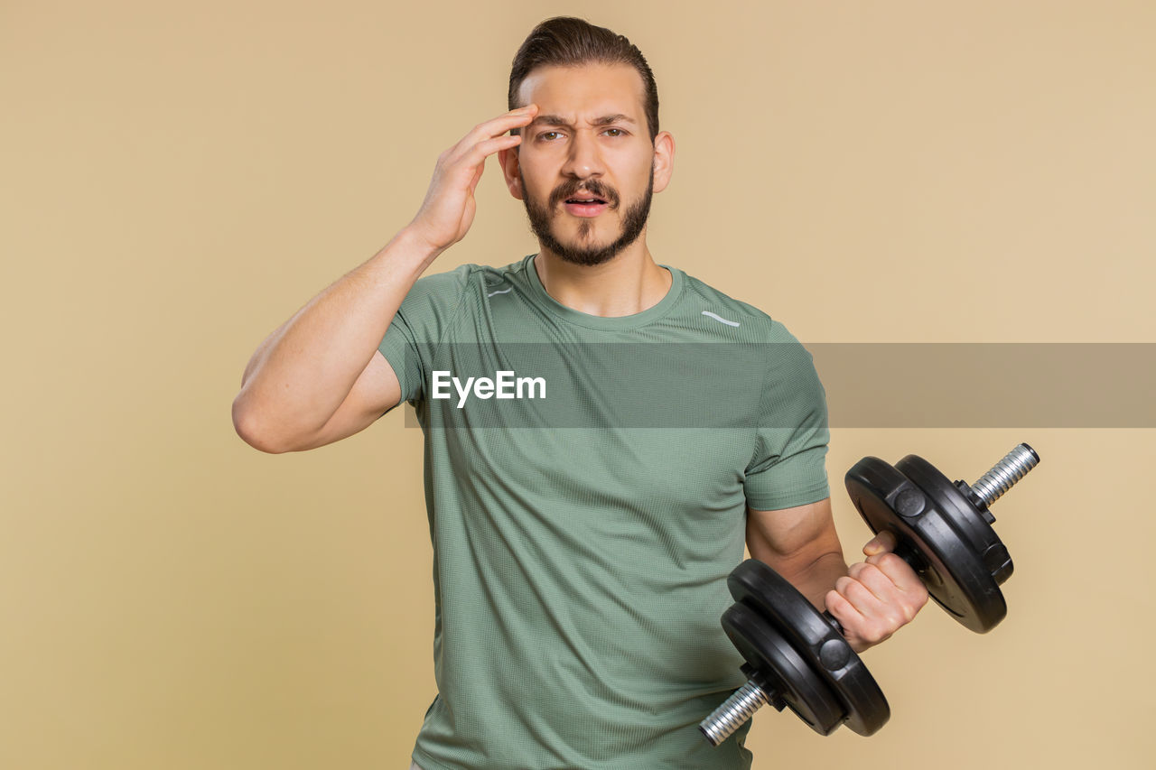 one person, adult, men, studio shot, indoors, colored background, portrait, waist up, casual clothing, arm, holding, copy space, standing, technology, lifestyles, front view, facial hair, young adult, beard, emotion, muscular build, exercising, sports training, vitality, sports, hand, communication, t-shirt, looking at camera, strength, athlete