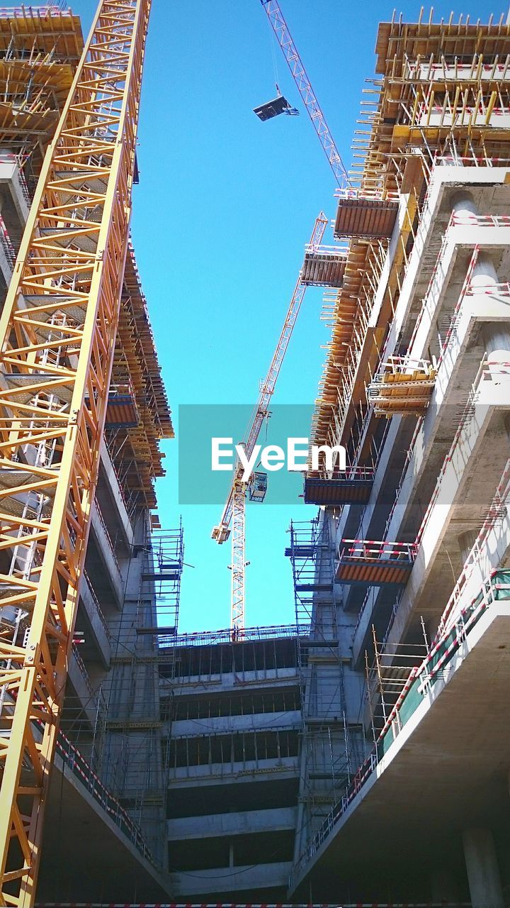 Low angle view of buildings under construction against blue sky