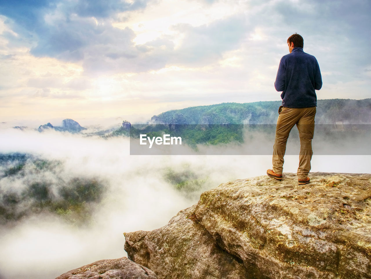 Photographer bend head check display of camera. man on cliff takes autumn beautiful photos of mist