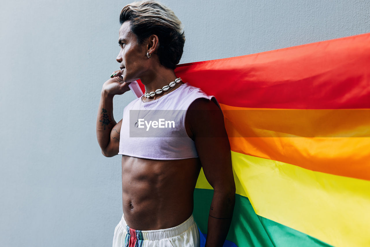 Gay man with rainbow flag against wall