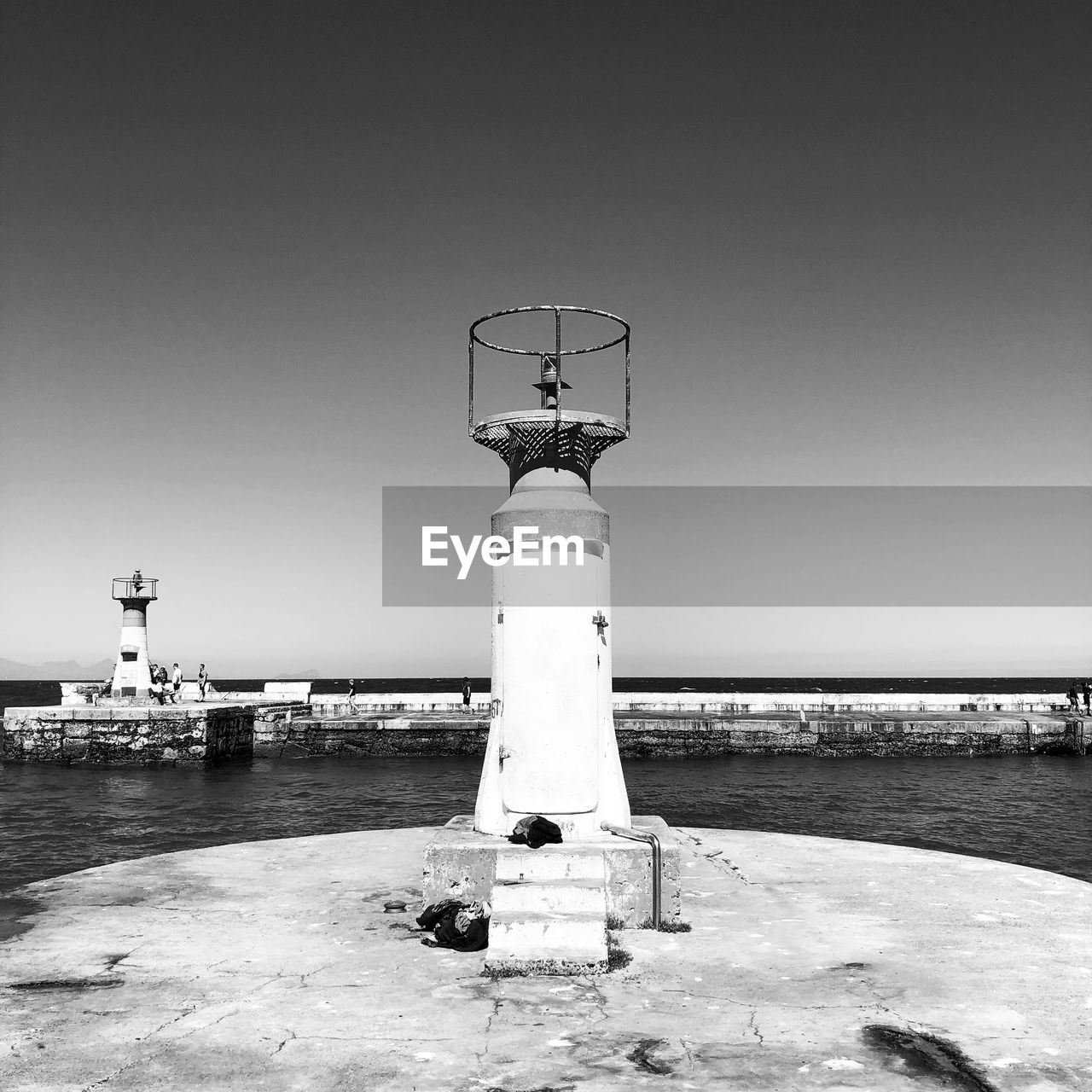 Lighthouse on pier by sea against clear sky